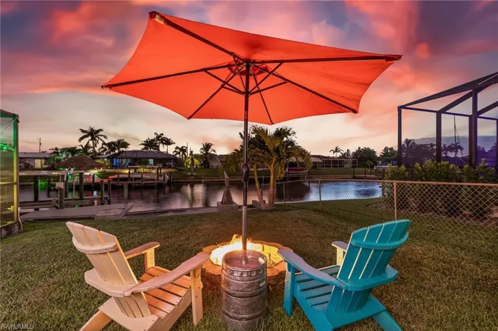 View of green lawn with a water view, glass enclosure, a fire pit, and a dock