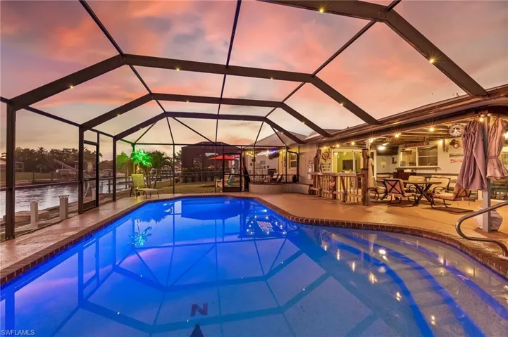 Pool at dusk featuring glass enclosure, an outdoor pool, a sunroom, and a patio