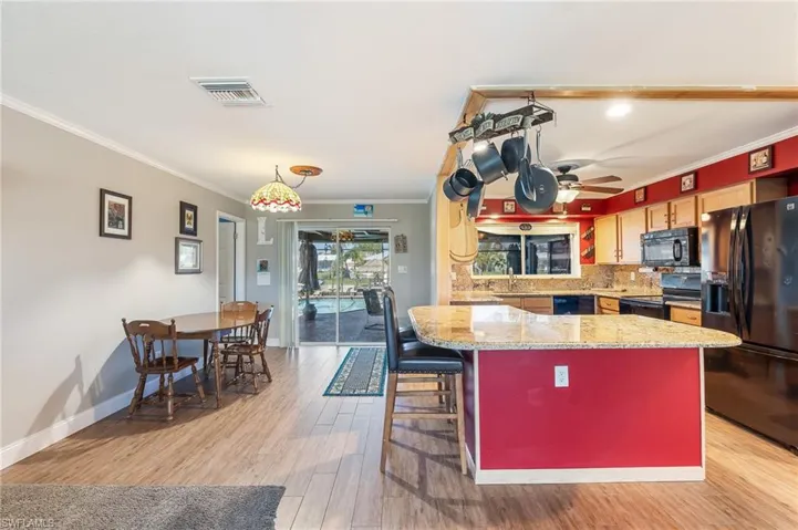 Kitchen with ornamental molding, black appliances, light wood-type flooring, tasteful backsplash, and light stone counters