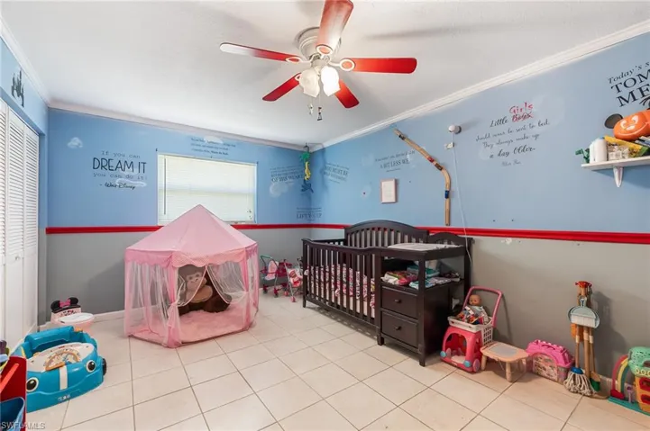 Bedroom with crown molding, ceiling fan, a nursery area, tile patterned flooring, and a closet