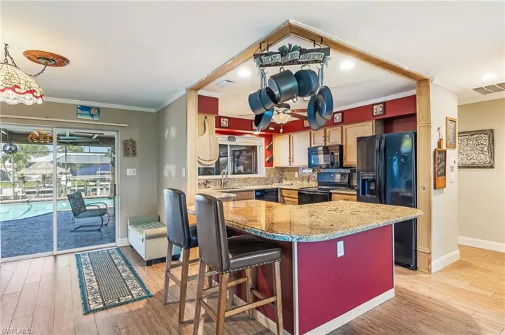 Kitchen featuring crown molding, light wood-type flooring, backsplash, black appliances, and light stone counters