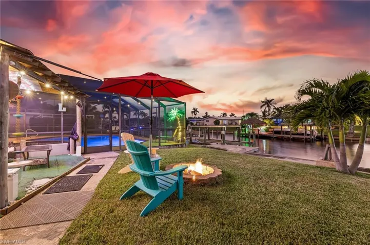 Playground at dusk featuring an outdoor pool, a fire pit, a water view, a sunroom, and a lawn