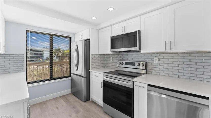 Kitchen featuring appliances with stainless steel finishes, light stone counters, white cabinets, and tasteful backsplash