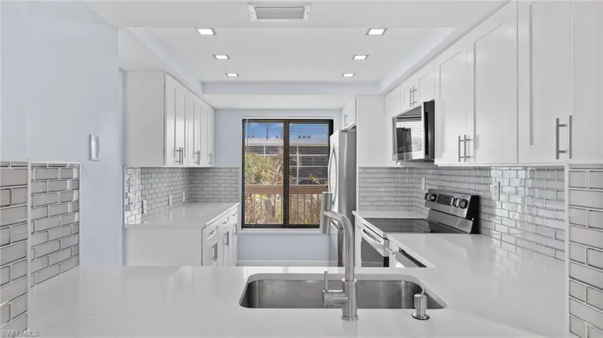 Kitchen with appliances with stainless steel finishes, white cabinets, light stone countertops, tasteful backsplash, and recessed lighting