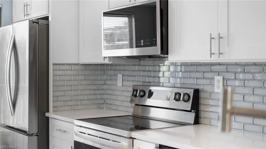 Kitchen with appliances with stainless steel finishes, decorative backsplash, white cabinets, and light stone countertops