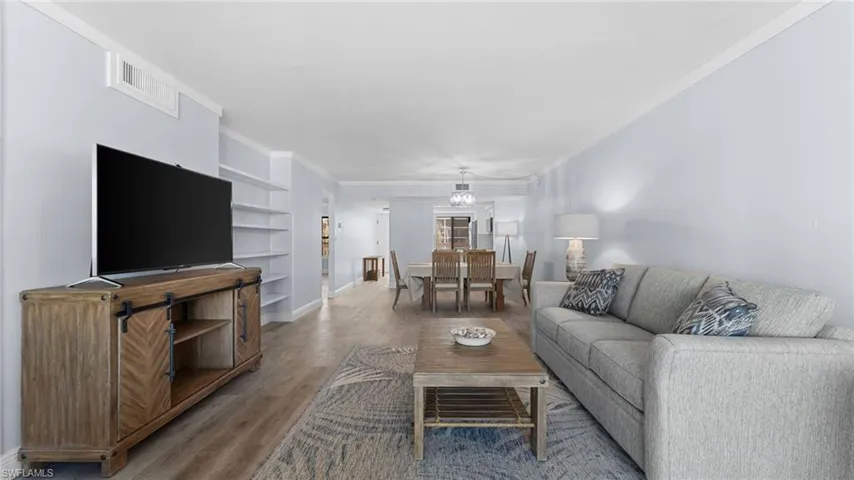 Living area with built in shelves, wood finished floors, and ornamental molding