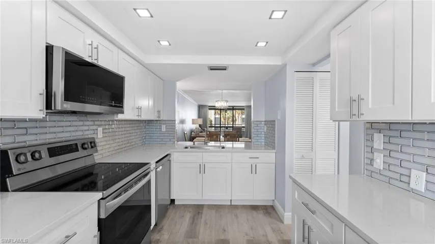 Kitchen featuring appliances with stainless steel finishes, light stone countertops, and white cabinetry
