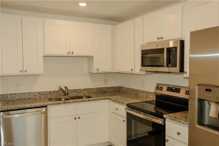 Kitchen featuring white cabinetry, speckled countertops, stainless steel appliances including a refrigerator, built-in microwave, range, and dishwasher