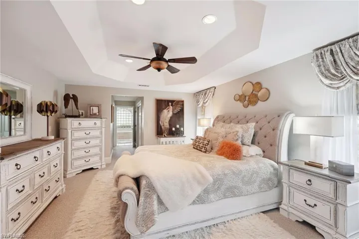 Bedroom with a raised ceiling, ceiling fan, and light carpet