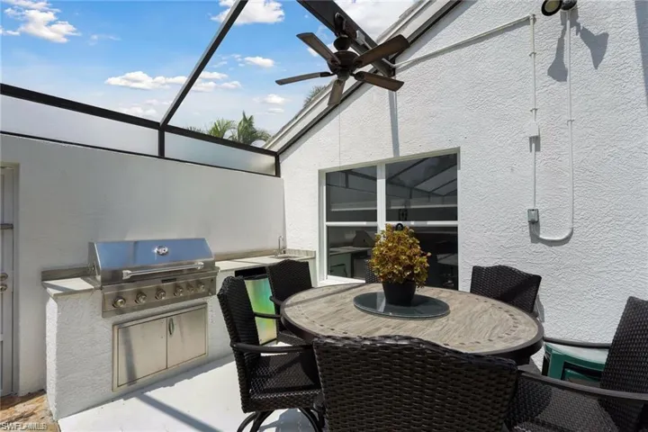 View of patio featuring exterior kitchen, a grill, glass enclosure, and ceiling fan