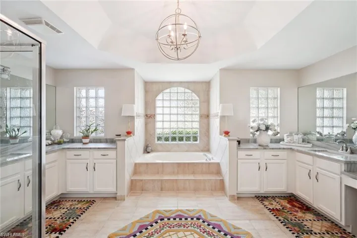 Bathroom with tile patterned floors, tiled tub, a notable chandelier, and vanity