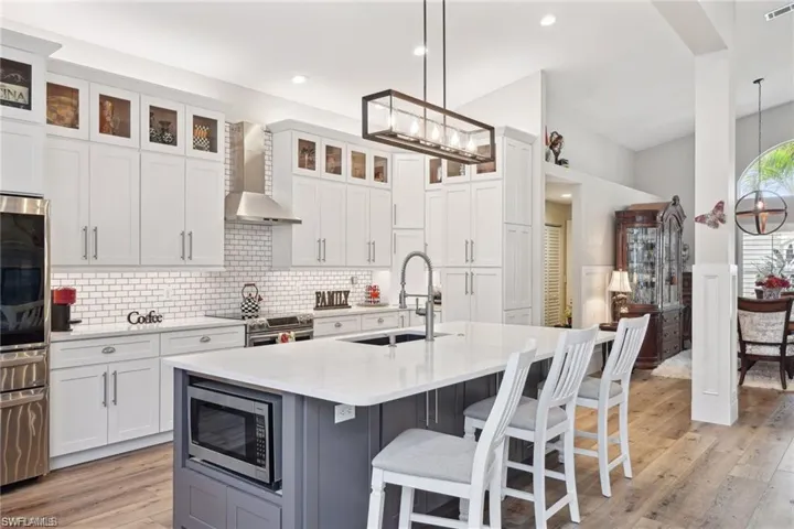 Kitchen with wall exhaust hood, vinyl prank flooring, an island with sink, stainless steel appliances, and sink
