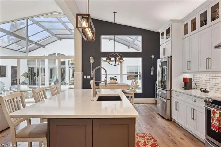 Kitchen with lofted ceiling, white cabinets, stainless steel appliances, and a center island with sink
