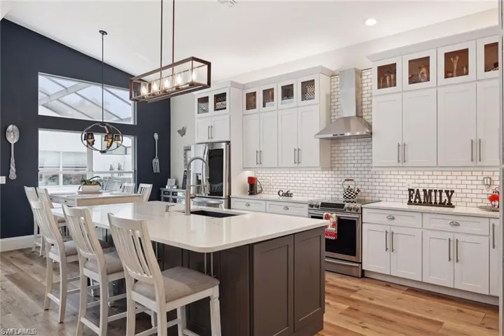 Kitchen featuring wall chimney exhaust hood, a notable chandelier, appliances with stainless steel finishes, an island with sink, and sink
