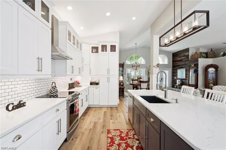 Kitchen with lofted ceiling, stainless steel appliances, white cabinetry, and wall range hood