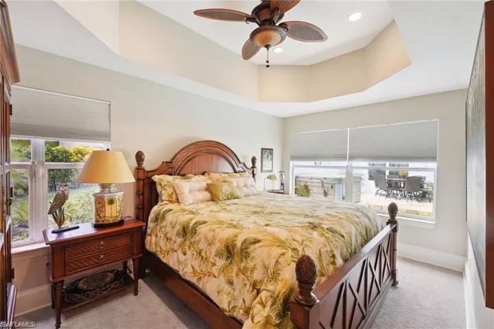 Carpeted bedroom featuring multiple windows, a raised ceiling, and ceiling fan