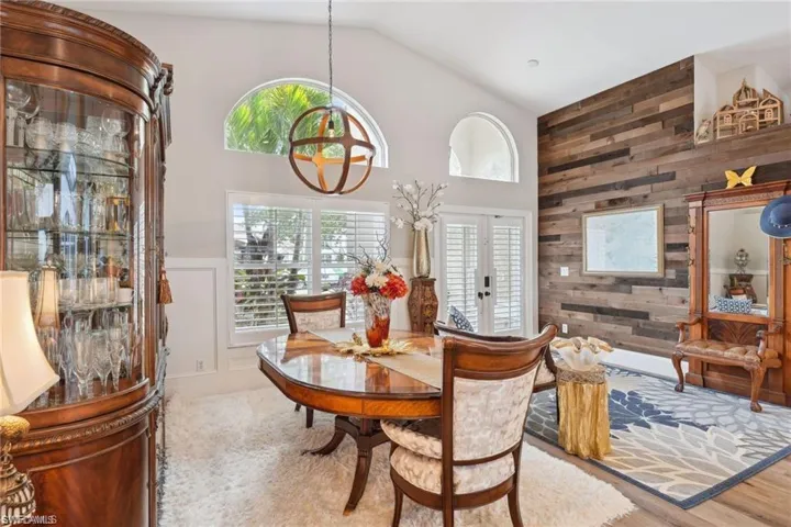Dining space with vinyl prank flooring, wooden walls, an inviting chandelier, french doors, and high vaulted ceiling