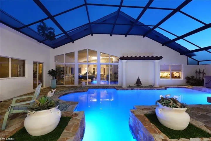 View of swimming pool with glass enclosure, pool water feature, and a patio area