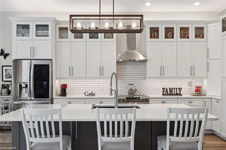 Kitchen with a breakfast bar area, stainless steel fridge with ice dispenser, an island with sink, hanging light fixtures, and wall  range hood