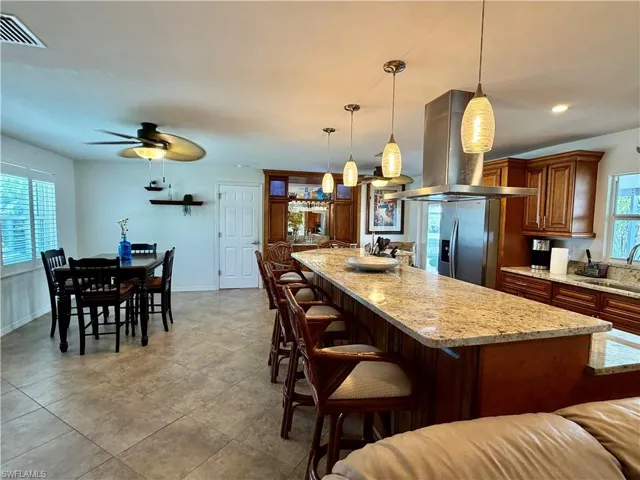 Open-concept kitchen and dining area featuring a large island with stone countertops, pendant lighting, stainless steel appliances, wood cabinetry, and tile flooring