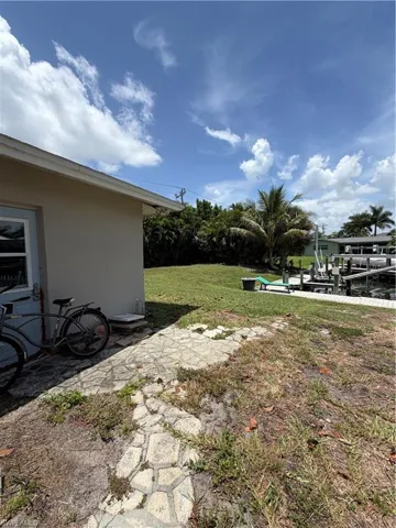 Waterfront property featuring a grassy expanse, mature palm trees, and a stone-patterned pathway