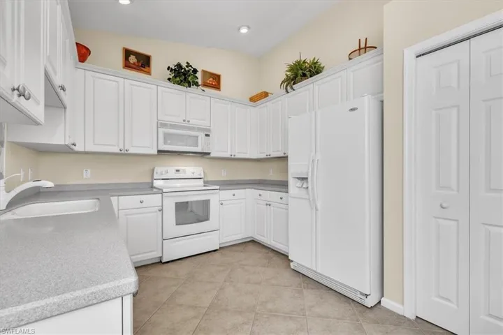 Kitchen featuring white appliances, white cabinets, light tile patterned floors, and recessed lighting