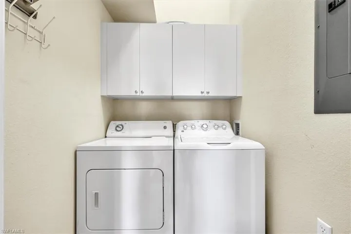 Laundry room with a textured wall, electric panel, cabinet space, and washer and clothes dryer