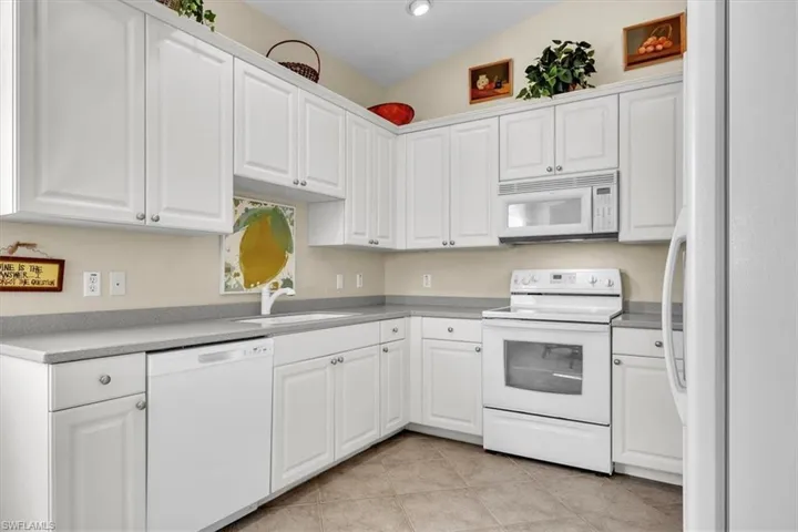 Kitchen with white appliances, white cabinets, light tile patterned floors, and light countertops