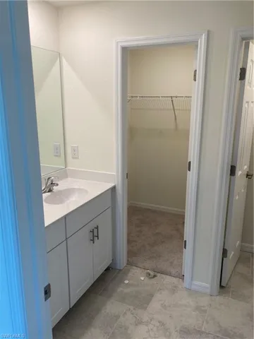 Bathroom featuring a walk in closet, vanity, and baseboards