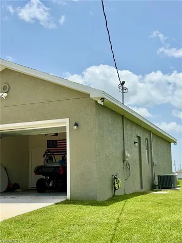 View of side of home featuring stucco siding, a yard, central air condition unit, concrete driveway, and a garage