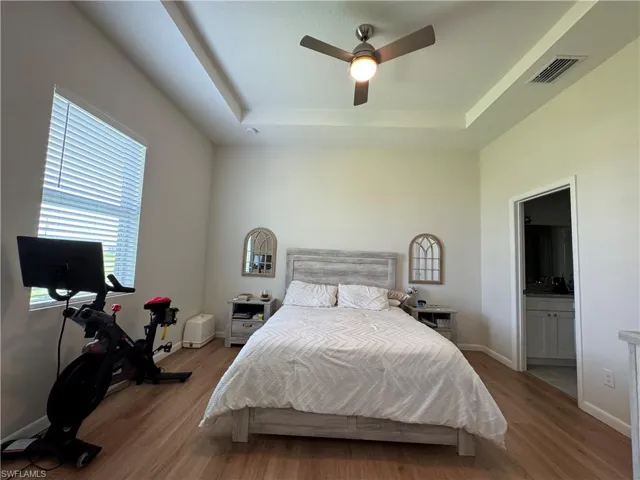 Bedroom with wood finished floors, a raised ceiling, a high ceiling, baseboards, and ceiling fan
