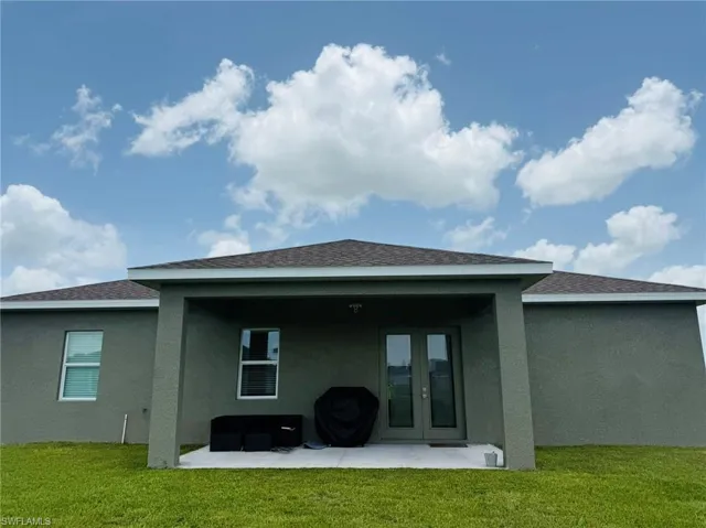 Rear view of property featuring stucco siding, a patio area, a lawn, and french doors