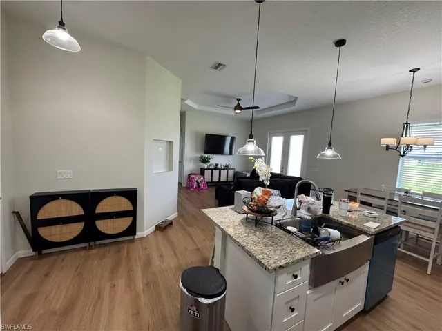 Kitchen with light wood-style floors, white cabinets, a kitchen island with sink, dishwasher, and a tray ceiling