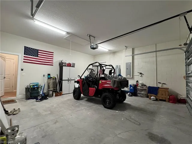 Garage with a garage door opener, electric panel, and concrete block wall