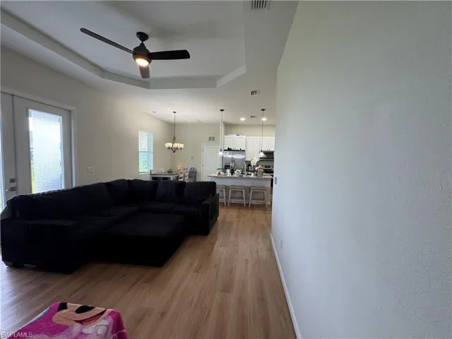 Living area with light wood-style floors, ceiling fan, baseboards, and a raised ceiling