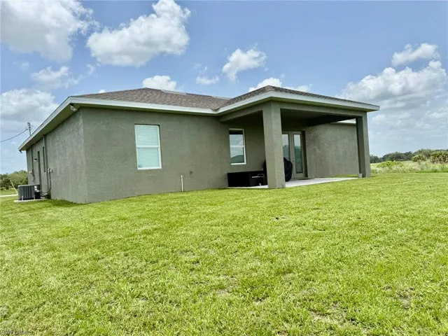 Back of property with central air condition unit, stucco siding, a patio area, and a yard