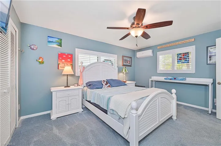 Bedroom with a wall mounted air conditioner, carpet floors, baseboards, and ceiling fan