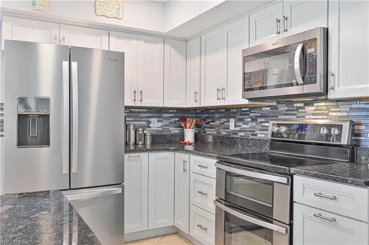 Kitchen with stainless steel appliances, tasteful backsplash, dark stone counters, white cabinets, and light tile patterned floors