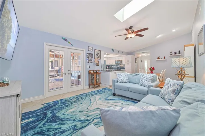 Living room with plenty of natural light, a skylight, lofted ceiling, french doors, and ceiling fan