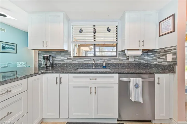 Kitchen with stainless steel dishwasher, a sink, backsplash, white cabinetry, and dark stone countertops