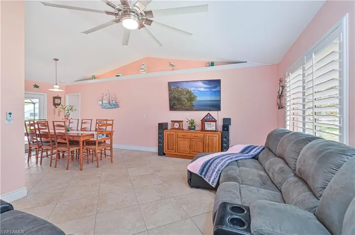 Living room featuring vaulted ceiling, ceiling fan, light tile patterned floors, and baseboards