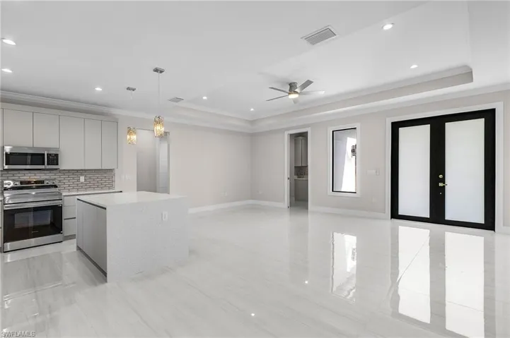 Kitchen with appliances with stainless steel finishes, backsplash, decorative light fixtures, a tray ceiling, and ornamental molding