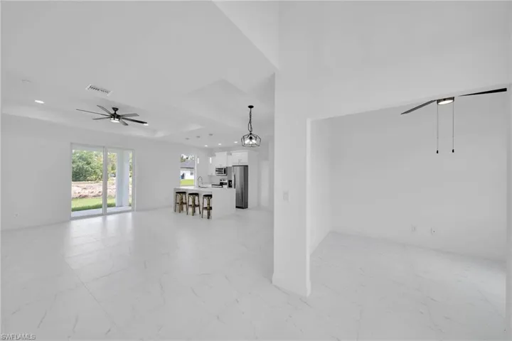 Unfurnished living room featuring a raised ceiling, sink, light tile floors, and ceiling fan with notable chandelier
