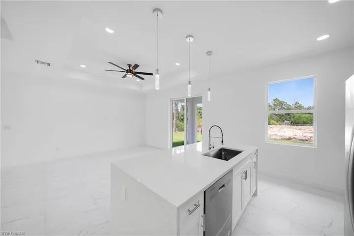 Kitchen with a center island with sink, ceiling fan, a tray ceiling, stainless steel dishwasher, and sink