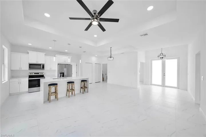 Kitchen with hanging light fixtures, a raised ceiling, an island with sink, appliances with stainless steel finishes, and light tile floors