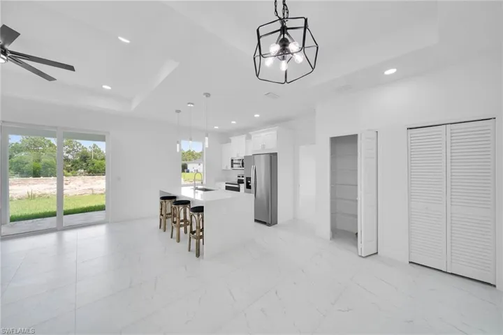 Kitchen with a kitchen island, hanging light fixtures, a raised ceiling, white cabinetry, and appliances with stainless steel finishes