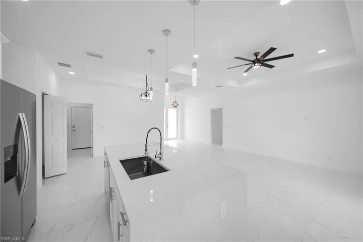 Kitchen featuring stainless steel fridge with ice dispenser, ceiling fan, a raised ceiling, sink, and light tile floors