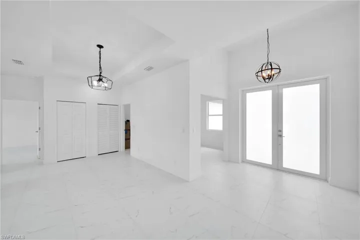 Spare room featuring french doors, a raised ceiling, light tile floors, a towering ceiling, and a chandelier