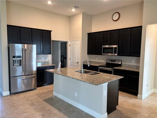 Kitchen with a kitchen island with sink, sink, a towering ceiling, light stone counters, and stainless steel appliances
