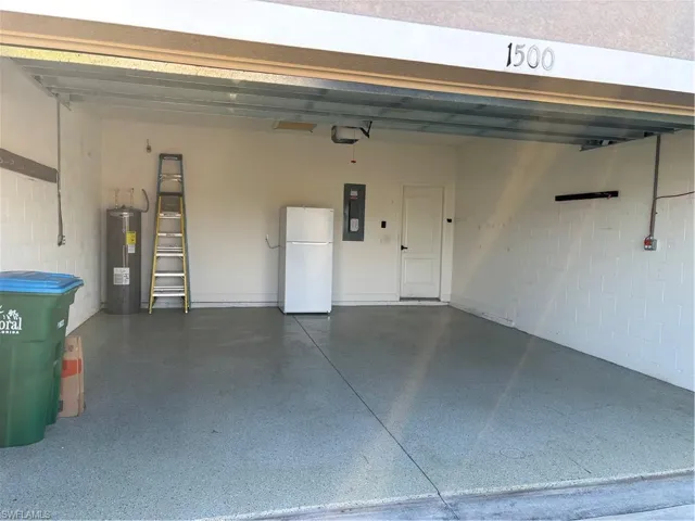 Garage with electric panel, white fridge, and water heater